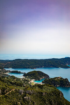 Aerial view of the turquoise waters of the Ionian Sea surrounding the lush green hills and rocky coastline of Corfu, Ionian Islands, Greece.