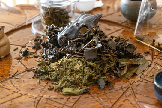 Pile of spent tea leaves with a ceramic dragon tea pet on a carved wooden tea tray