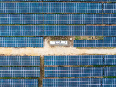 Aerial view of a large scale solar photovoltaic power plant with rows of blue panels and a maintenance structure along a dirt path in Central Seberang Perai, Penang, Malaysia.