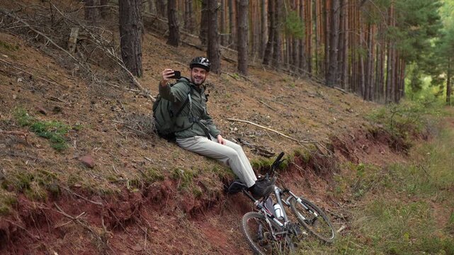 Cyclist takes a break in the forest, enjoying nature and checking his phone