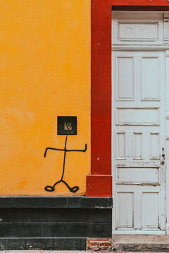 Arte callejero minimalista con un monigote dibujado sobre una pared amarilla junto a una puerta blanca