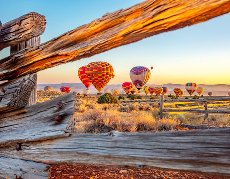 Hot air balloons floating during sunset in desert landscape with rustic wooden frame foreground