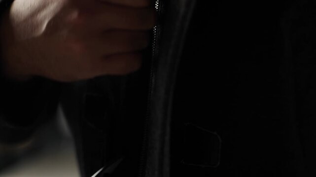 Male hands buttoning up dark winter coat in dim room, getting dressed and preparing to go outside, close up view, detail, slow motion