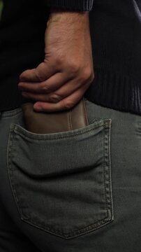 Male hand taking out leather wallet from back pocket of jeans pants, close up view, vertical view, slow motion