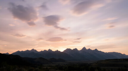 Obraz premium Stunning sunset view over the majestic Teton mountain range peaks under a soft pastel colored cloudy sky