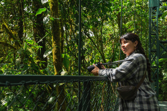 Woman exploring lush rainforest on hanging bridge with camera