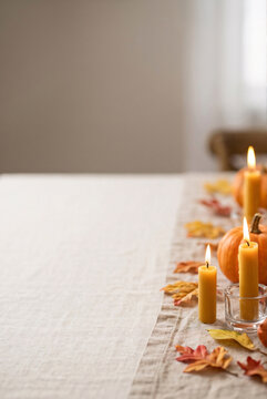 Vertical view of warm glowing candles and autumn leaves arranged on a cozy table