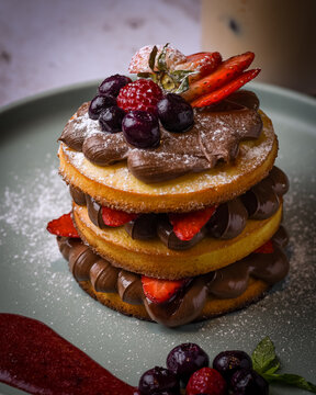 Torre de panqueques con crema de chocolate frutillas ar&aacute;ndanos y coulis de frutos rojos servida en plato