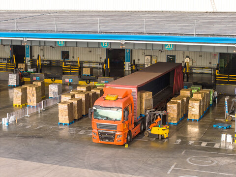 orange truck unloading cargo at warehouse loading dock with forklift