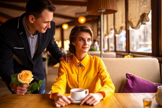 Man presenting a yellow rose to a woman in a restaurant