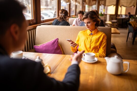 Woman using her smartphone at a restaurant table while a man gestures