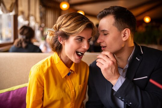 Smiling man feeding a dessert to a woman with a spoon