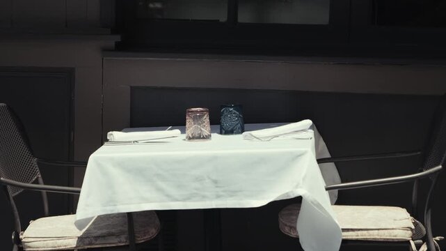 Restaurant table set with crystal glasses and white tablecloth in dim lighting, elegant dining setup, video footage.