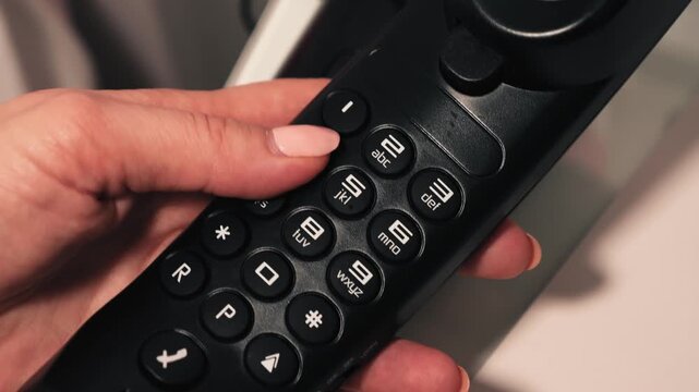 Close-up of a hand pressing buttons on a hotel room telephone handset. Concept of hotel communication, customer service, business travel, and hospitality.