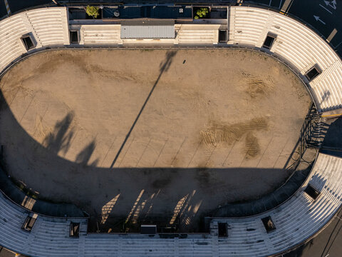 Aerial view of the oval-shaped Feria Ganadera with tiered concrete seating and a sandy central area, casting long shadows in Santo Domingo, Distrito Nacional, Dominican Republic.
