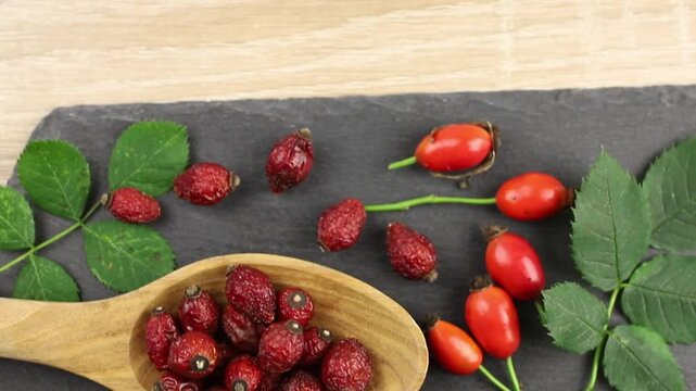 Dried Rosa canina, the dog rose or rose hip berries on wood spoon, decorated with fresh berries and green rose hip leaves, studio composition.