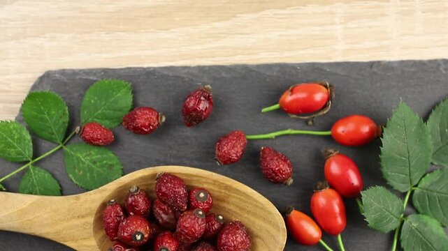 Dried Rosa canina, the dog rose or rose hip berries on wood spoon, decorated with fresh berries and green rose hip leaves, studio composition.