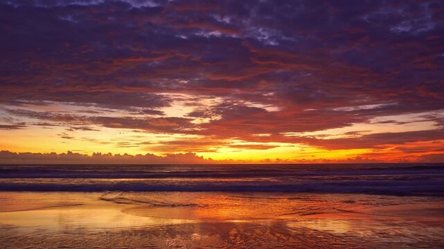A soft golden glow spreads through the sky, blending with hues of pink and lavender as the ocean mirrors the evening fire. The peaceful beach becomes a stage for nature&rsquo;s quiet masterpiece.
