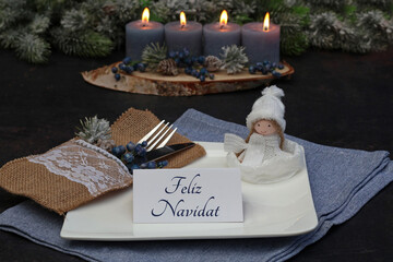 Obraz premium Mesa navideña decorada de manera festiva con un plato cuadrado, una servilleta de yute, un pequeño angelito navideño y una tarjeta de lugar con la inscripción en español «Feliz Navidad».