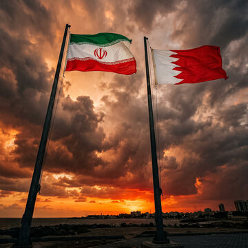 iran and bahrain flags wave on tall flagpoles against a bright sunset sky over the coast