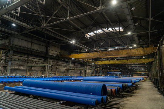 Large ductile iron pipe factory filled with coated waterworks pipes, overhead cranes and heavy manufacturing infrastructure for municipal pipeline production.