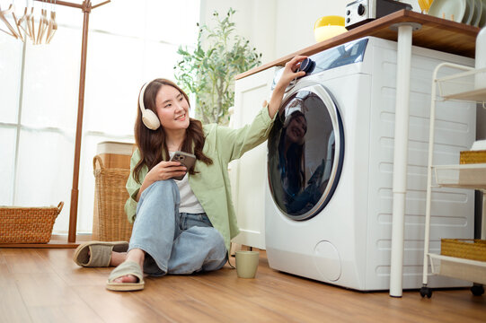 Asian Woman Using Smartphone and Listening to Music While Doing Laundry