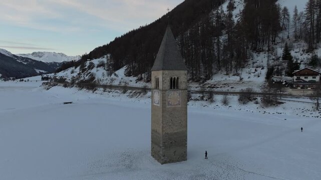 Aerial view of the historic submerged bell tower of Curon rising from the frozen Reschensee lake in Graun im Vinschgau, Trentino-Alto Adige, Italy.