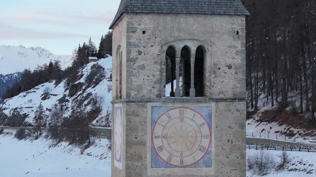 Aerial view of the historic sunken church tower of Curon surrounded by snow-covered mountains and frozen landscape in Graun im Vinschgau, Trentino-Alto Adige, Italy.