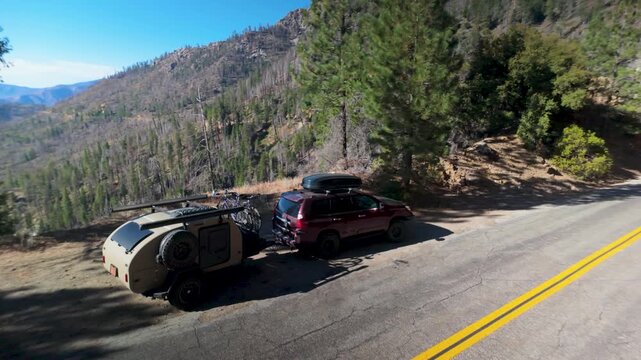 An SUV pulls a teardrop camper trailer on a road in the Sierra mountains, approaching Sherman Pass in California.