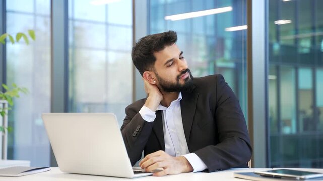 Tired businessman in suit suffers from neck pain while working on laptop at workplace in business office. Unwell male worker massaging touching sore muscles, has fatigue or posture problem.