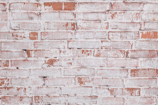 Close-up view of an old whitewashed brick wall featuring exposed red brick, distressed paint, rough masonry, and irregular vertical surface marks. The aged architectural texture 