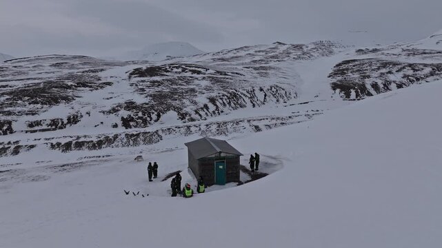 Aerial view of a small cabin in a vast snowy landscape with people standing outside in Pyramiden, Svalbard, Svalbard and Jan Mayen.