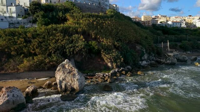 Rodi Garganico Gargano Puglia Italy drone golden sunrise white town. Low angle aerial pan over rocky beach, ancient trabucco fishing platform, waves sound 4K.