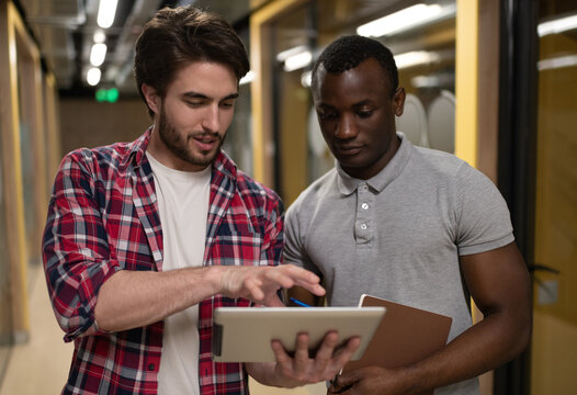 Diverse men using tablet in  in hallway of modern workspace