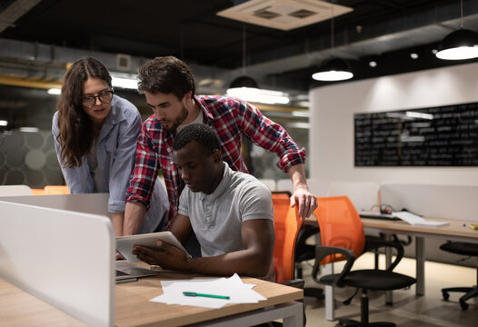 Young people helping black colleague with project in coworking