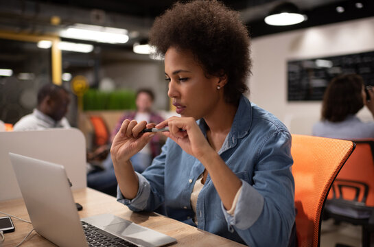Smart black woman reading data from laptop in coworking space