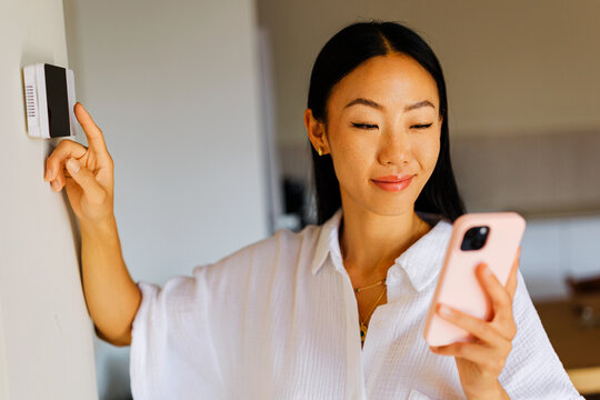 Woman checking thermostat while holding smartphone