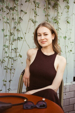 A woman sits at a caf&eacute; table backed by trailing vines