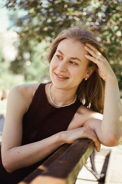 A woman leans on a park bench and smiles into the distance