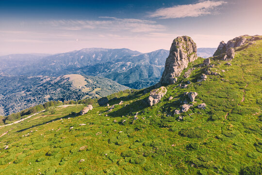 Green alpine meadow with dramatic limestone rock formation Babin Zub rising above layered mountain valleys at summer sunrise. Scenic nature background - Stara Planina park in Serbia, Balkans.