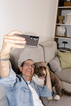 Senior man taking selfie with curly collared dog at home with flash