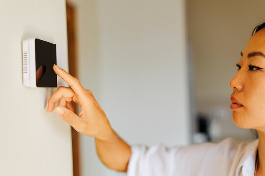 Woman adjusting smart home thermostat for ideal living temperature