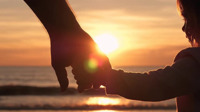 Silueta de las manos de un padre y su hijo unidas con ternura frente al atardecer en el agua, simbolizando amor, protecci&oacute;n y familia.
