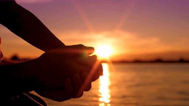 Silueta de las manos de un padre y su hijo unidas con ternura frente al atardecer en el agua, simbolizando amor, protecci&oacute;n y familia.
