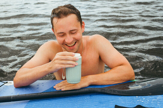 Man Enjoying Drink coffee While swimming near Paddle Board in Water
