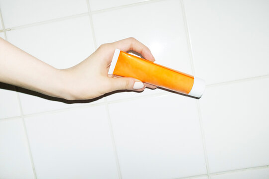 Hand holding orange skincare beauty product tube in front of tile wall