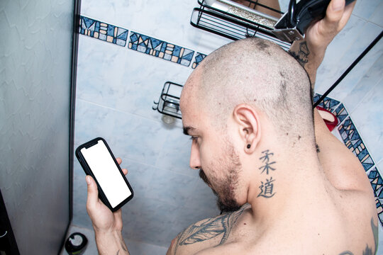 Man Shaves Head While Holding Phone in a Bathroom Shower