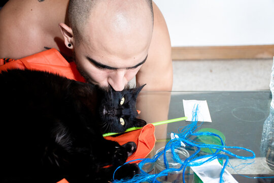 Man Kisses Black Cat While Sitting at Table