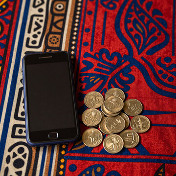 mobile payment concept with feature phone and coins on patterned