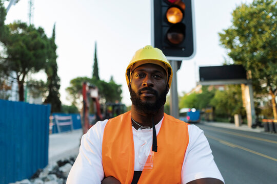 Black construction worker posing with arms crossed on urban site